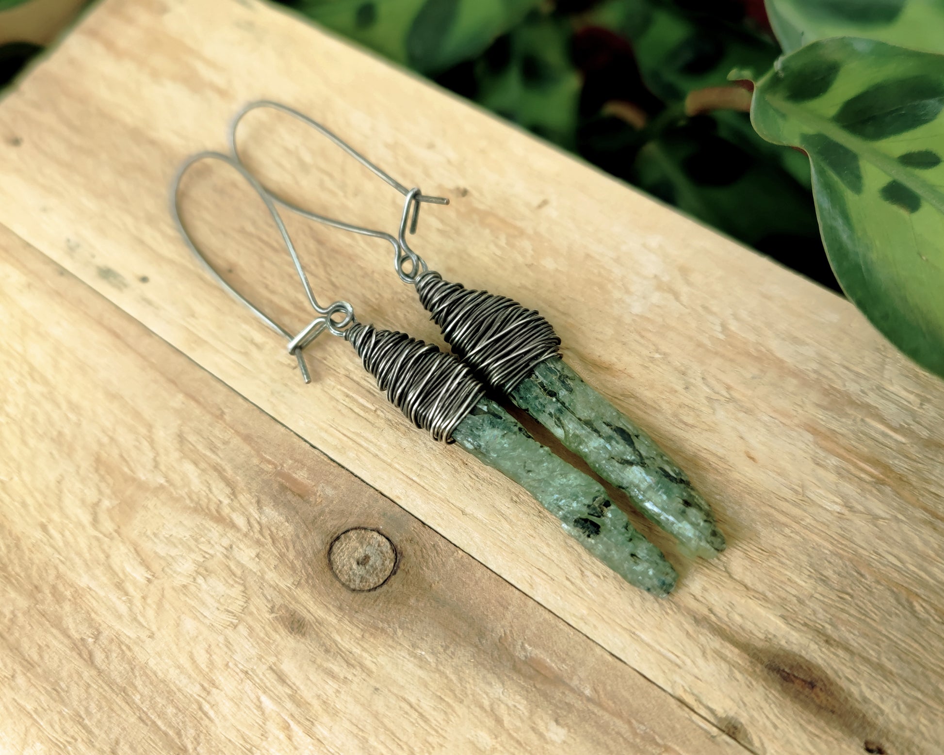 Silver green kyanite earrings resting on a wood board.