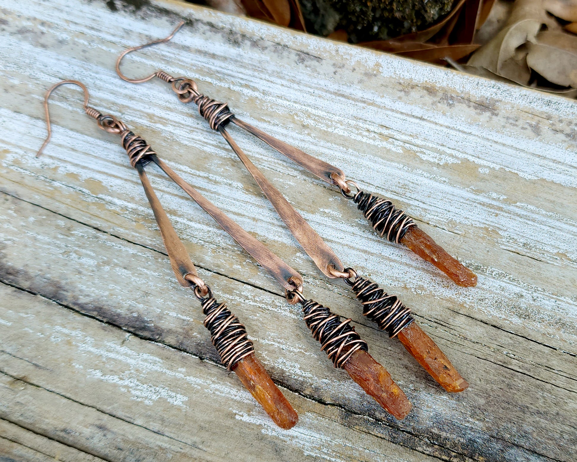 Orange kyanite earrings on a wood background.