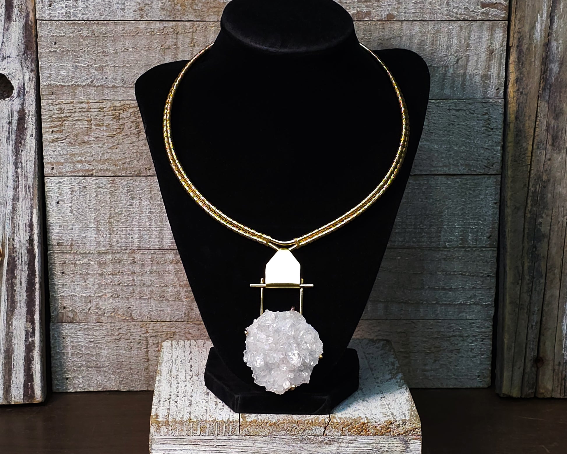 Arkansas quartz yellow brass torque necklace on a black display stand.