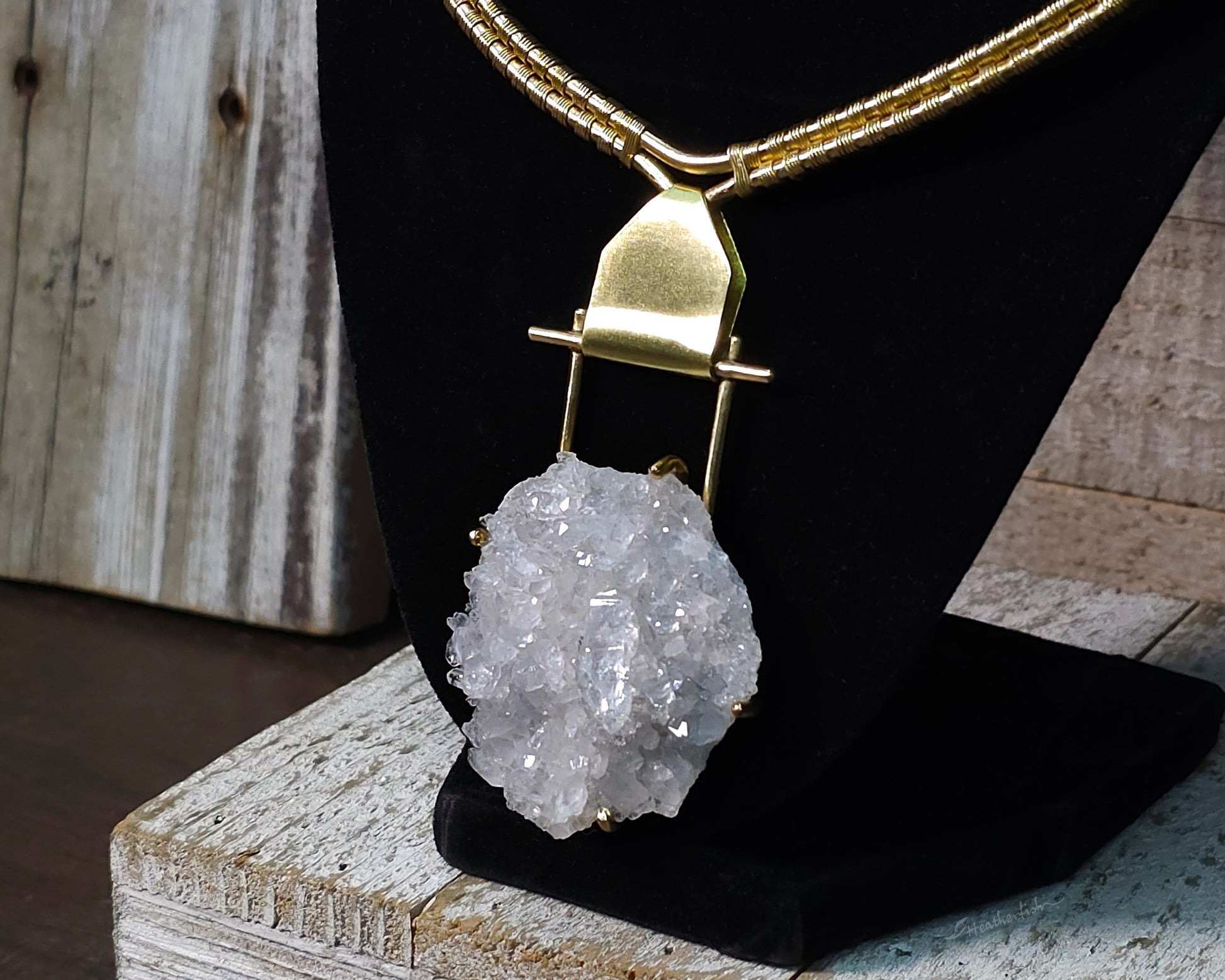 Arkansas quartz yellow brass torque necklace on a black display stand.