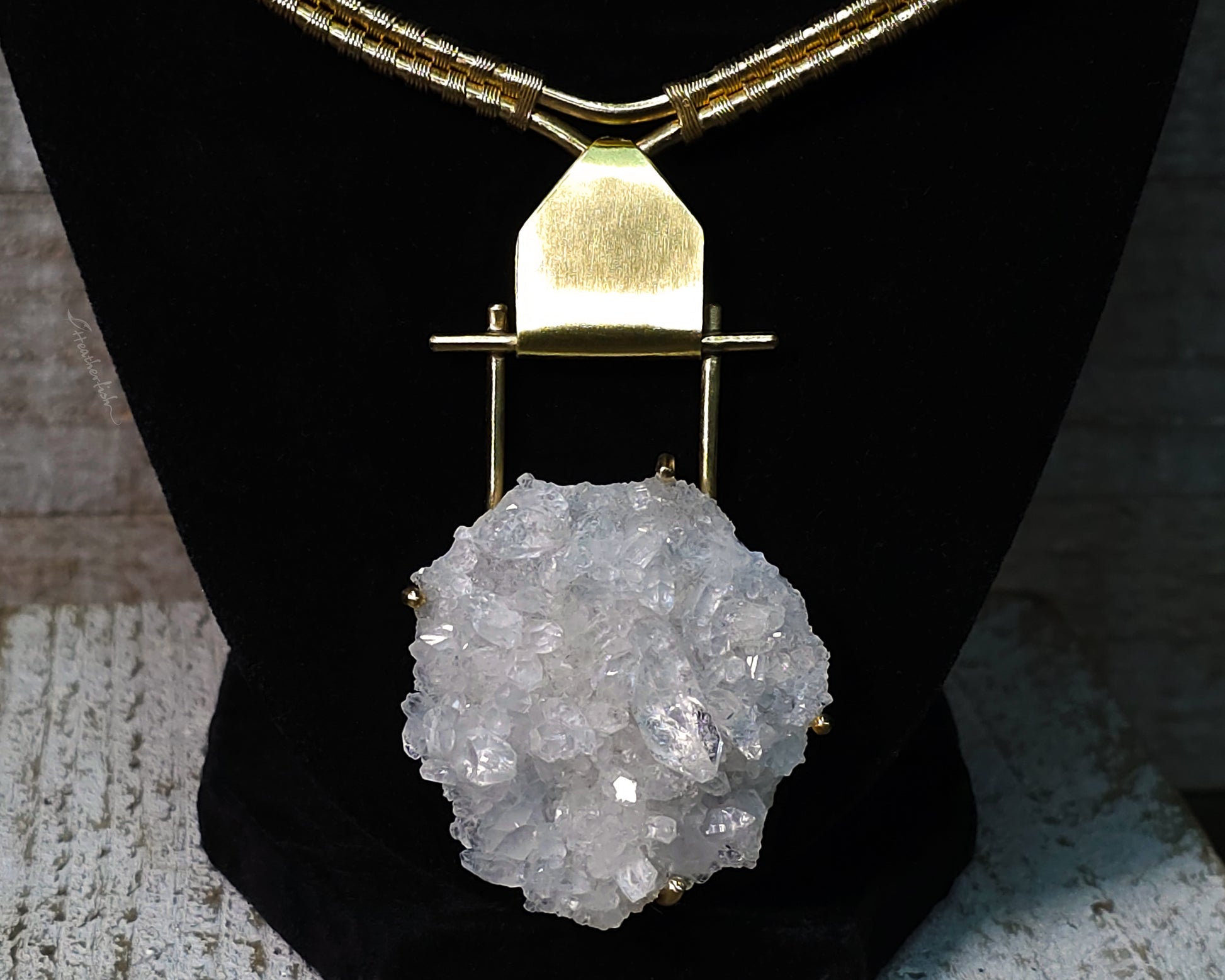 Arkansas quartz yellow brass torque necklace on a black display stand.