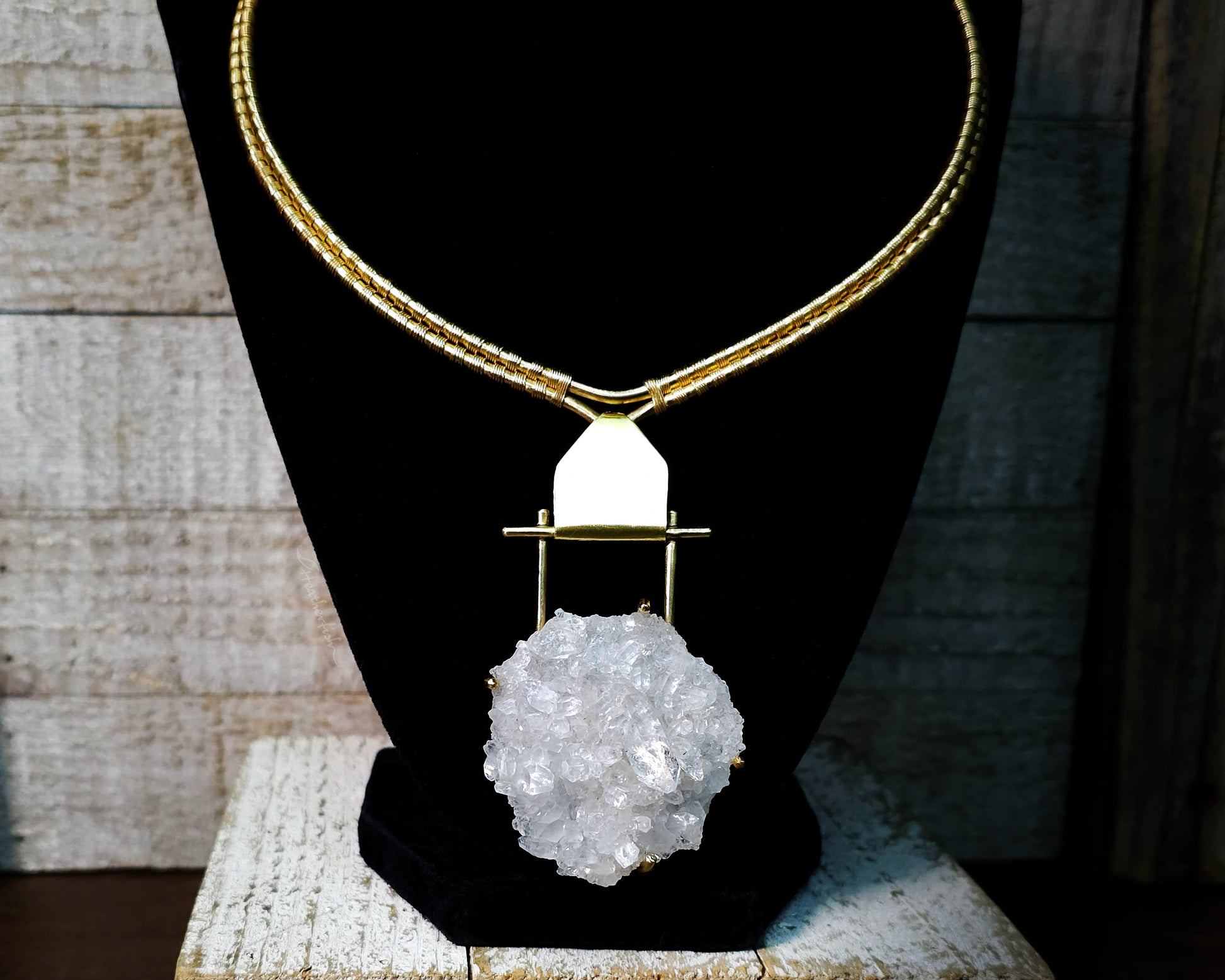 Arkansas quartz yellow brass torque necklace on a black display stand.