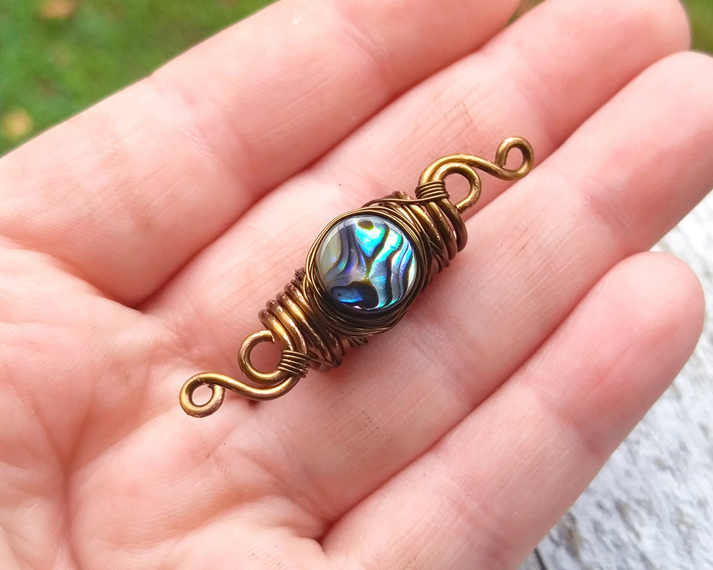 Abalone dread bead held in hand for reference.