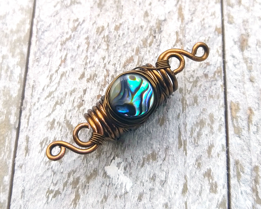 Abalone dread bead on a white wood background.