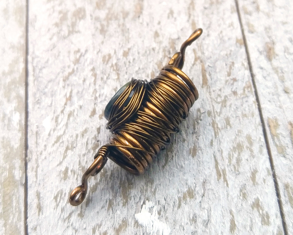 Abalone dread bead on a white wood background.