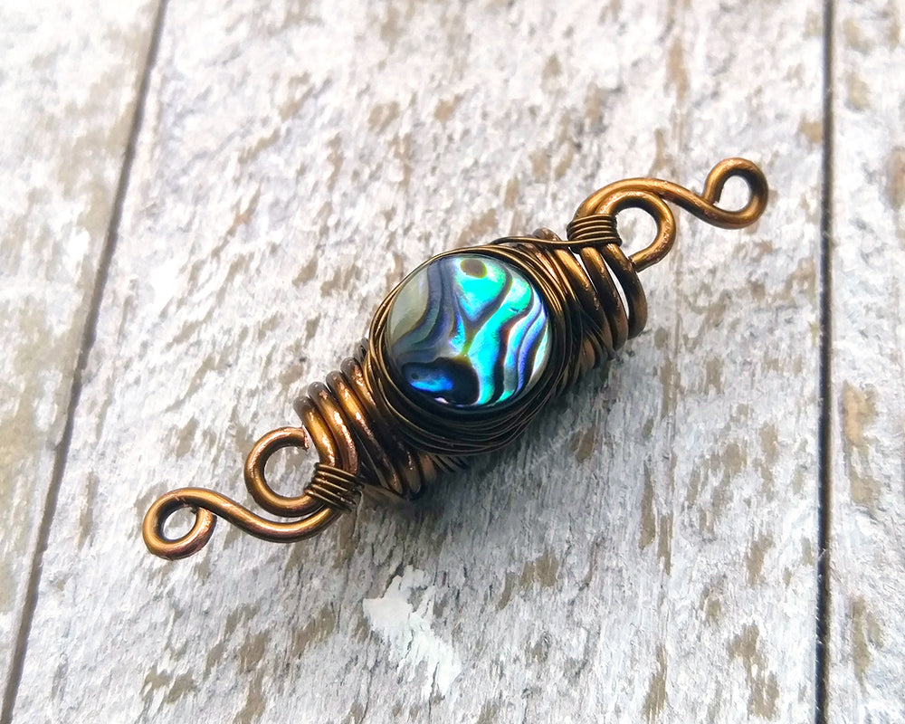 Abalone dread bead on a white wood background.