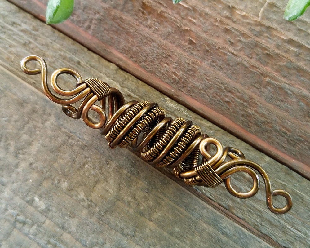 Close up view of a Fancy Woven Filigree Dread Bead on a wooden background.