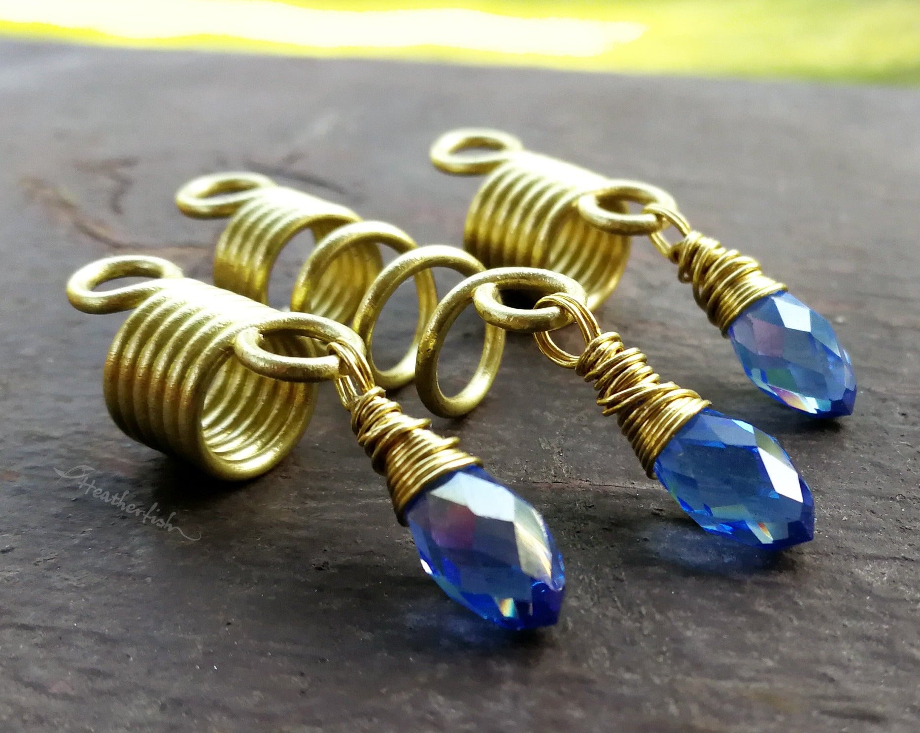 Side view of a set of 3 dread beads with periwinkle glass accents on a painted wood background.