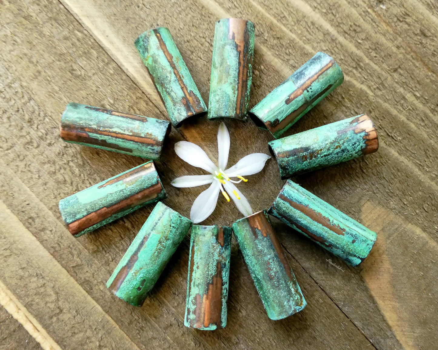 A top view of Green Patina Copper Tube Beads on a wooden background.