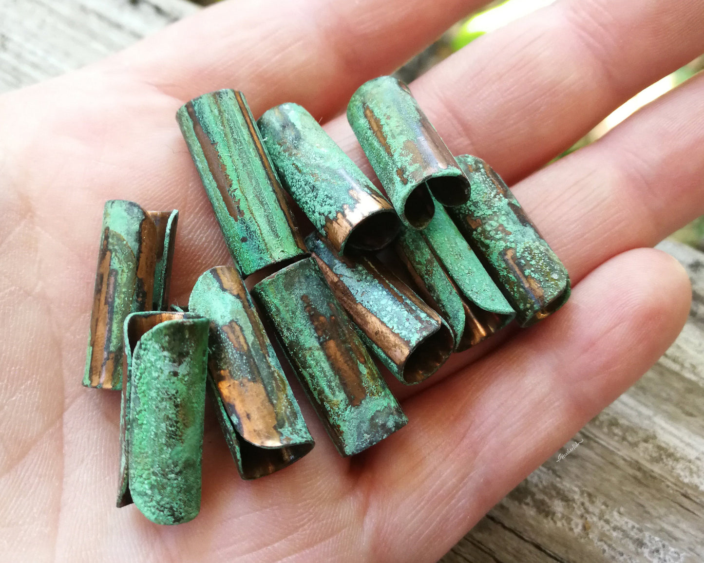 A top view of Green Patina Copper Tube Beads in hand.