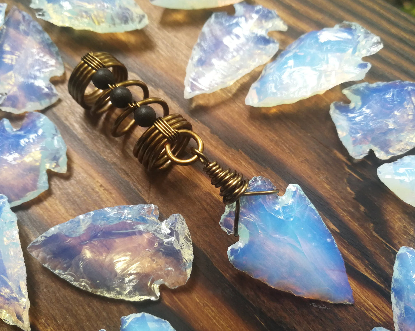 A close up view of a Opalite Glass Arrowhead Dread Bead on a wooden background.