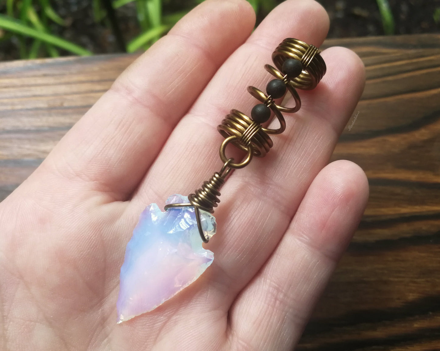 A top view of a Opalite Glass Arrowhead Dread Bead in hand.
