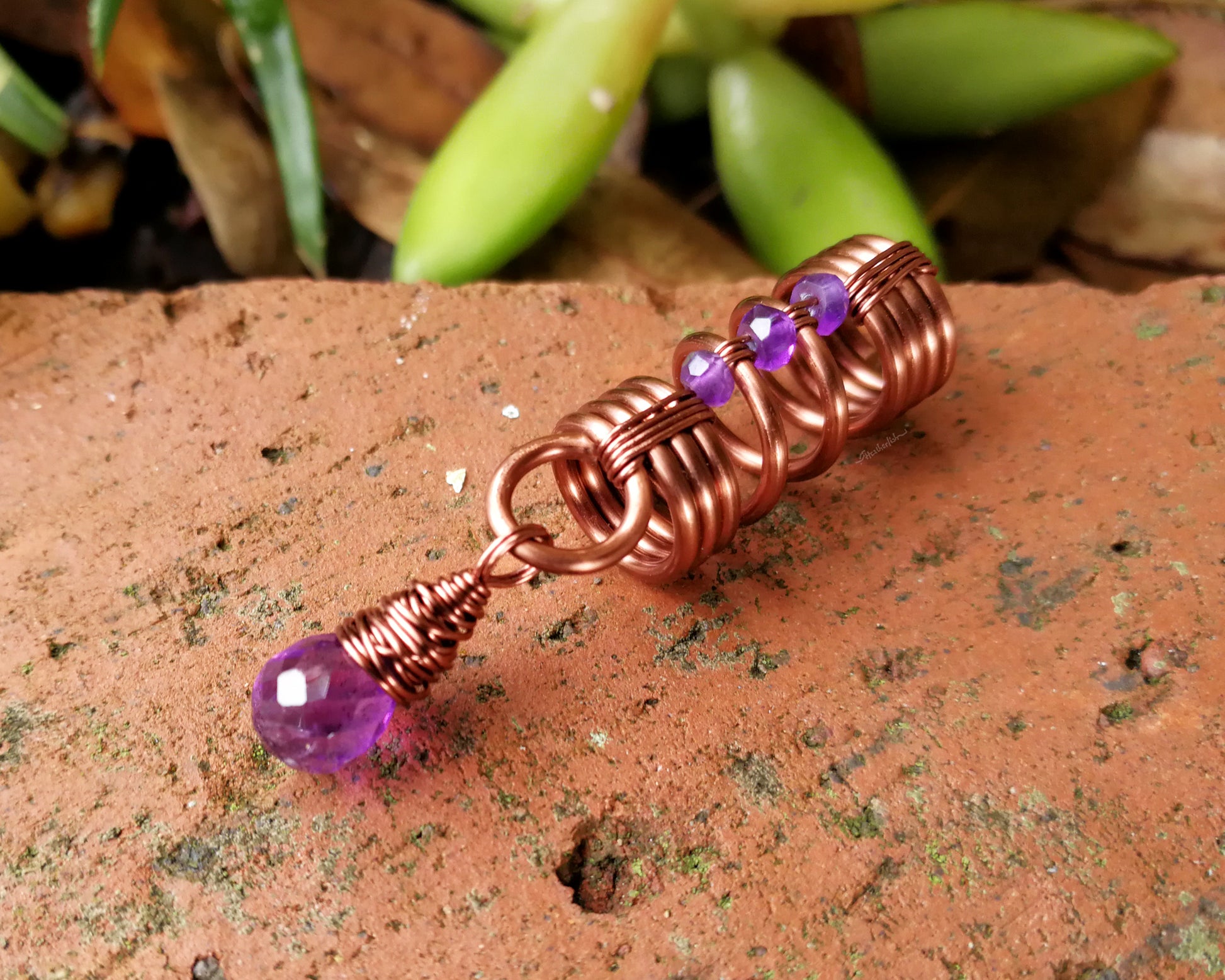 An amethyst dread bead on a brick background.