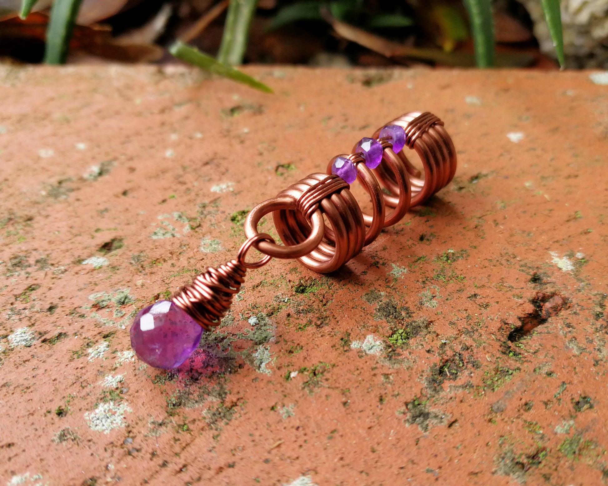 An amethyst dread bead on a brick background.