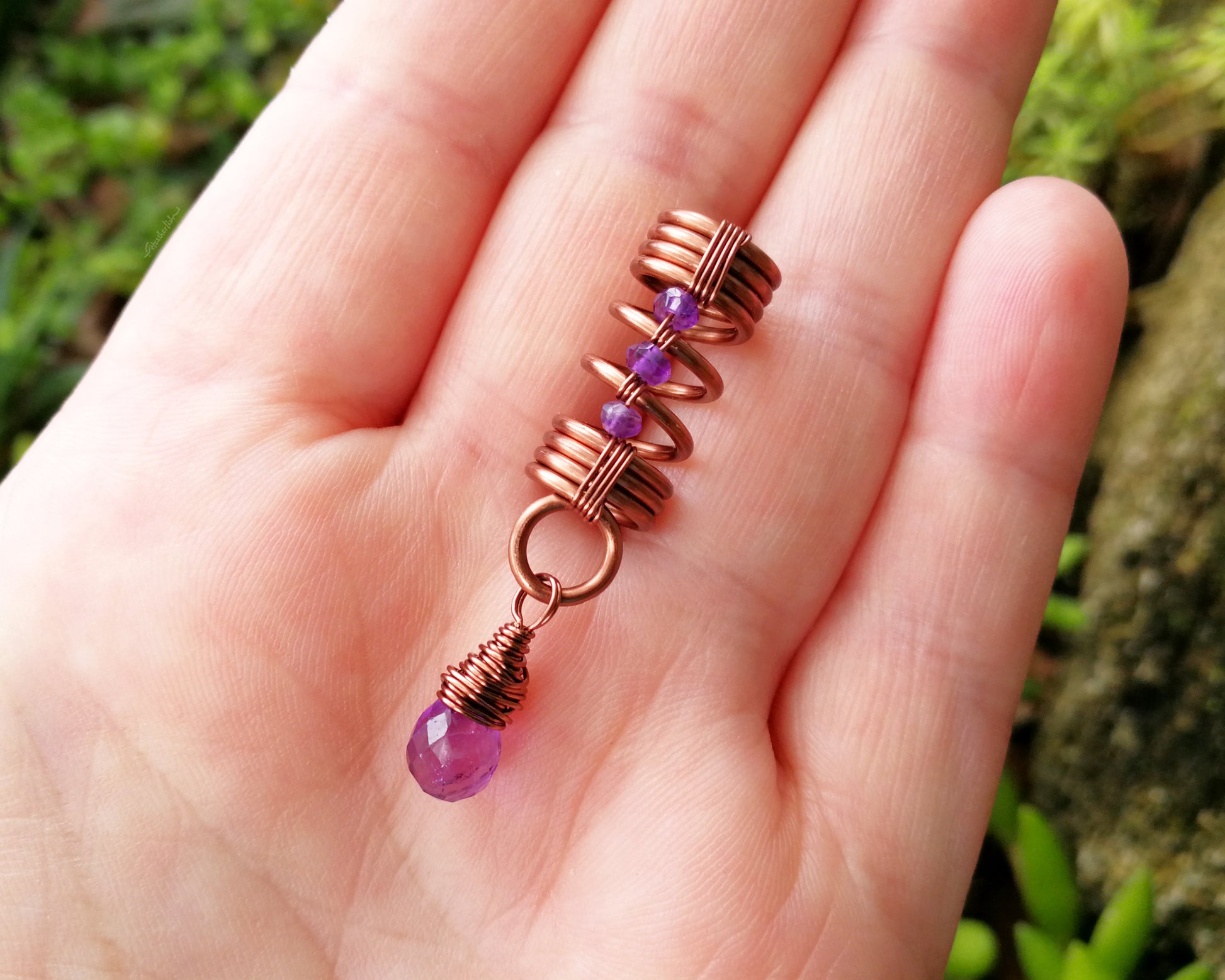 An amethyst dread bead held in a hand to show scale.