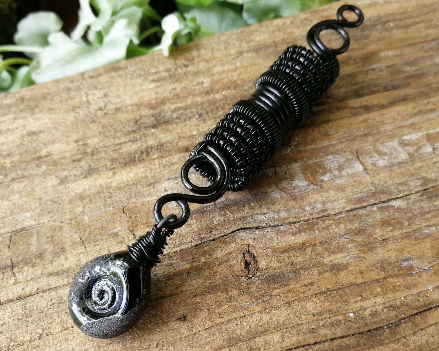 Black stardust glass dread bead on a wood backdrop.