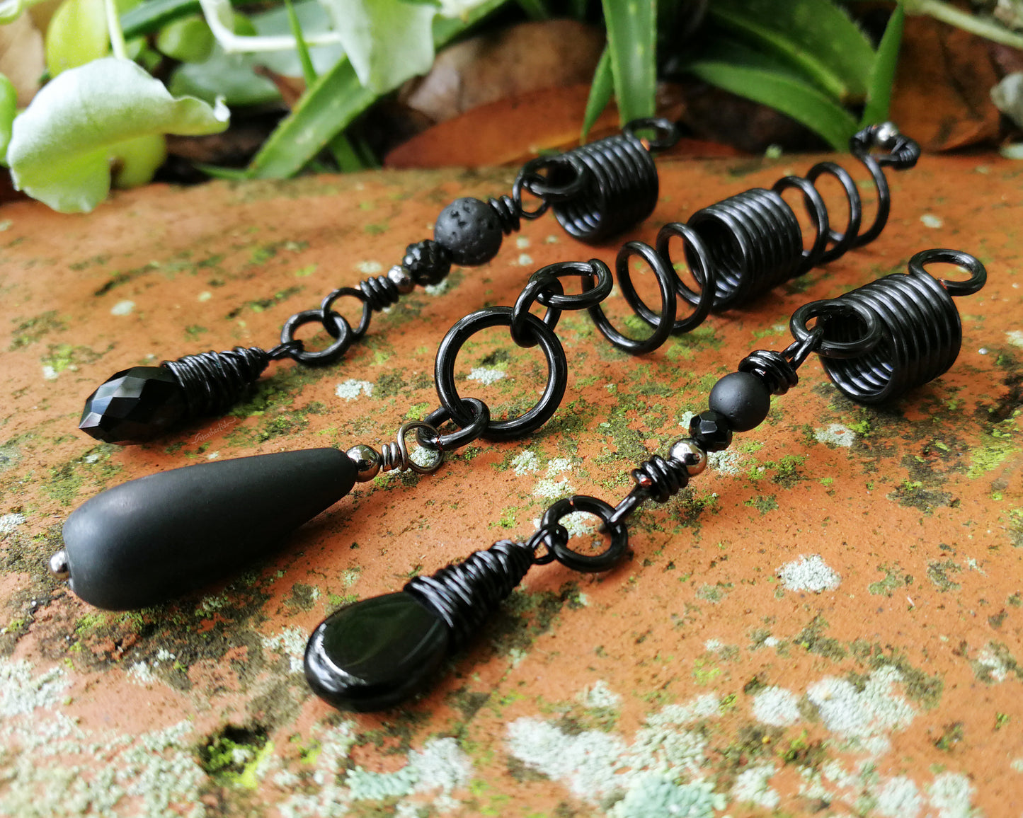 Set of three black dreadlock beads on a red brick backdrop.