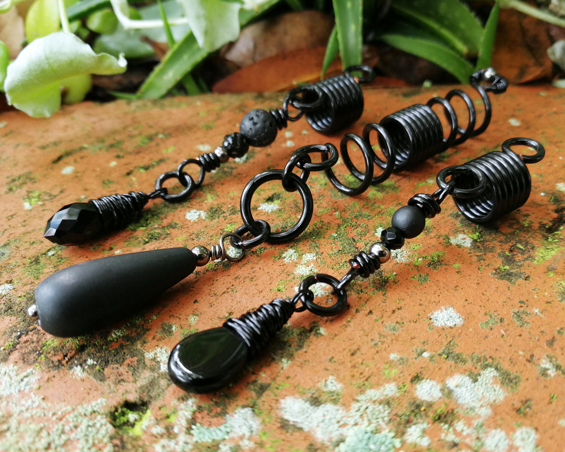 Set of three black dreadlock beads on a red brick backdrop.