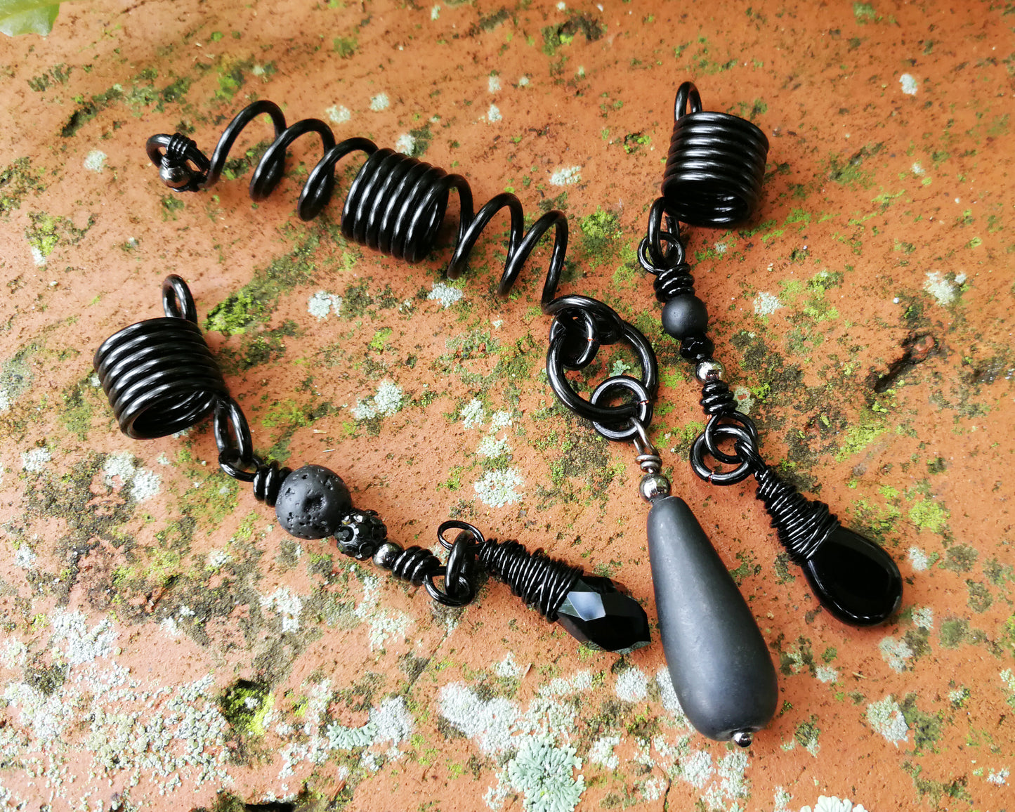 Set of three black dreadlock beads on a red brick backdrop.