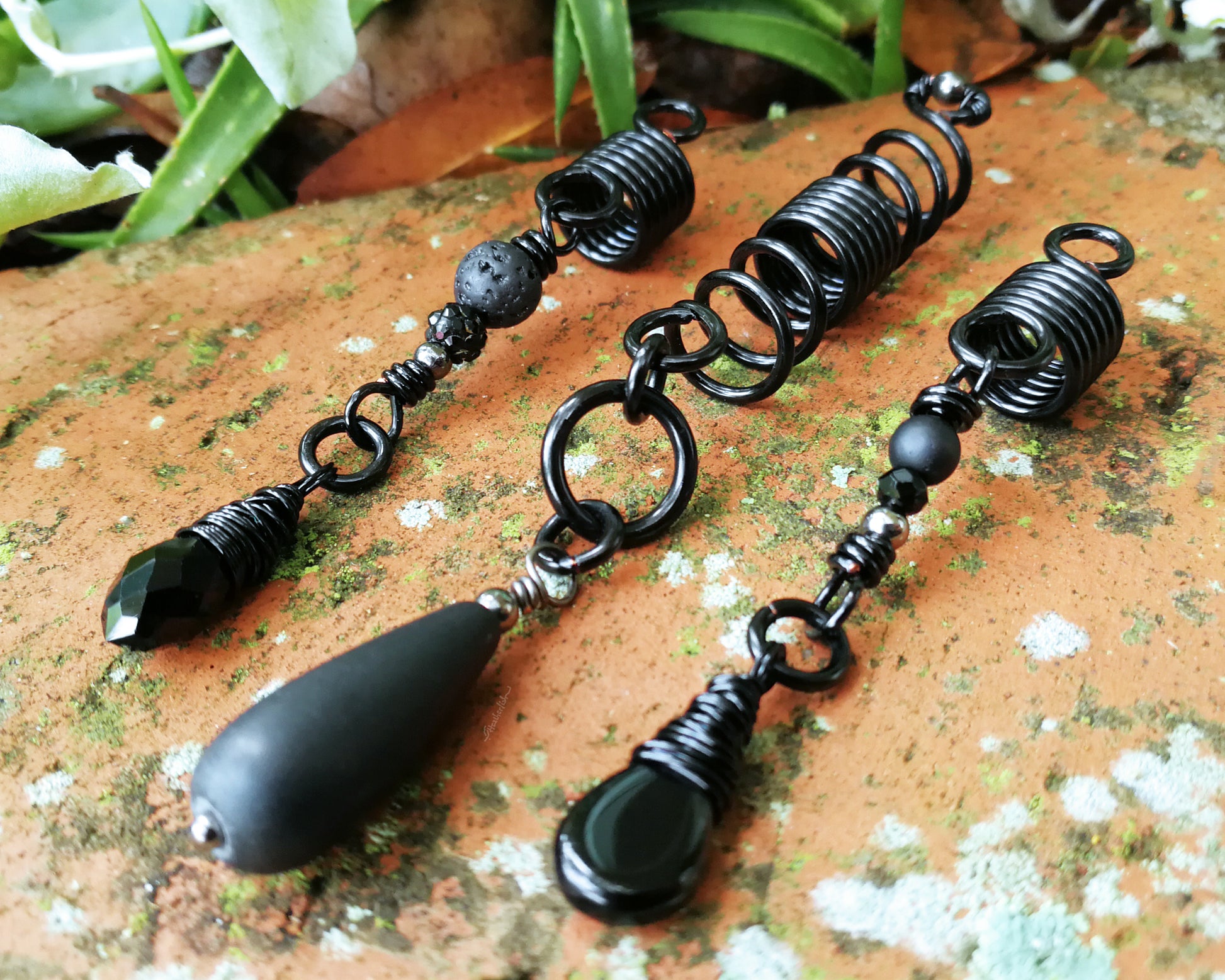 Set of three black dreadlock beads on a red brick backdrop.