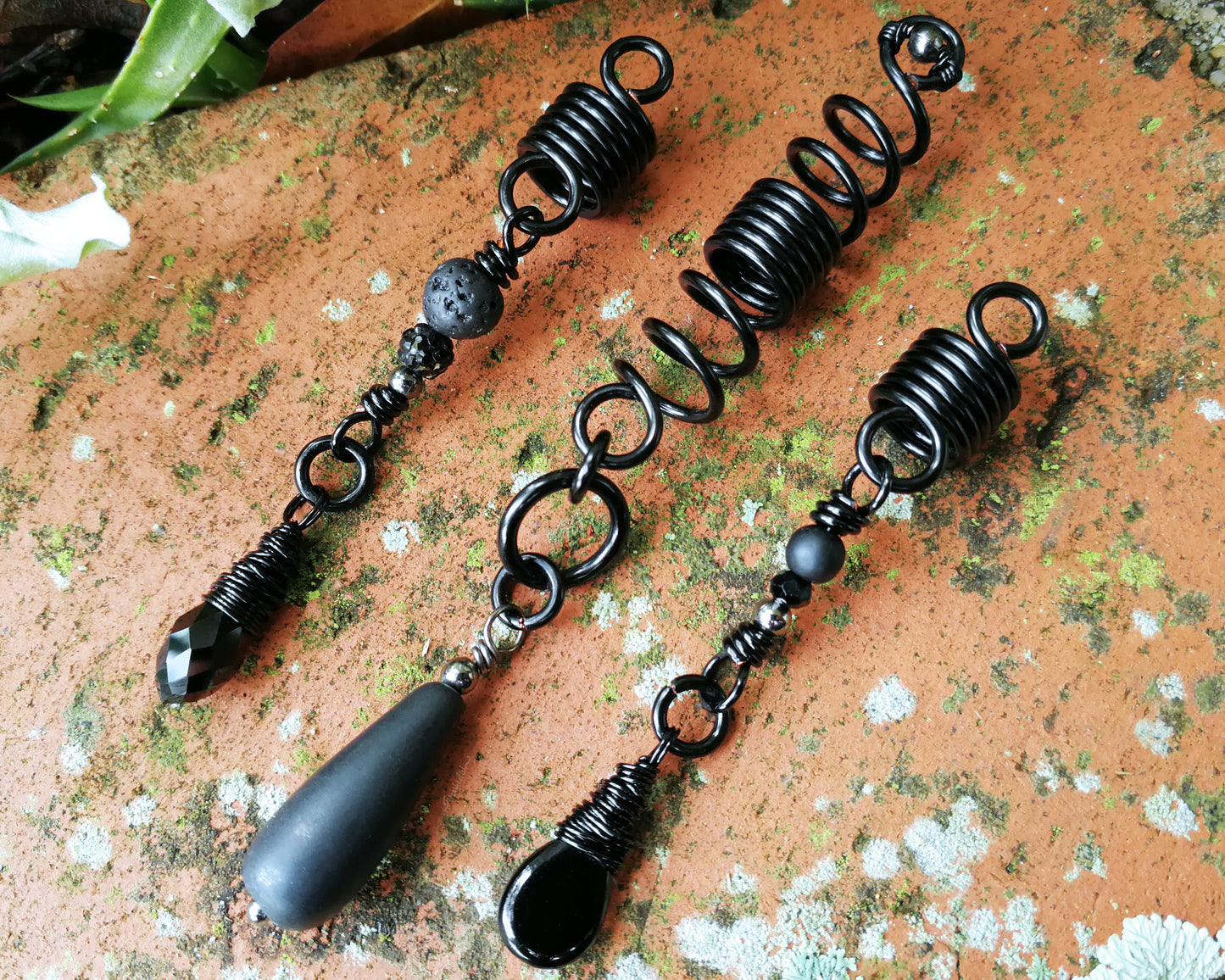 Set of three black dreadlock beads on a red brick backdrop.