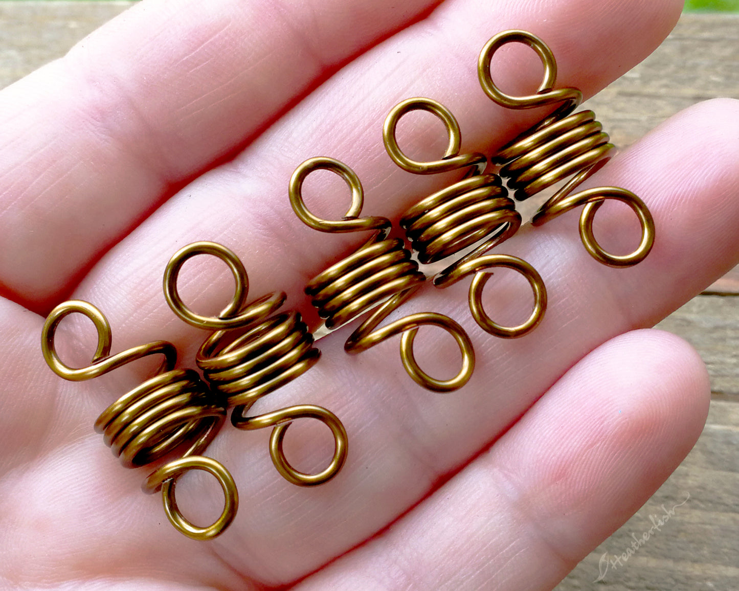 A set of 5 hair beads held in a hand to show scale.