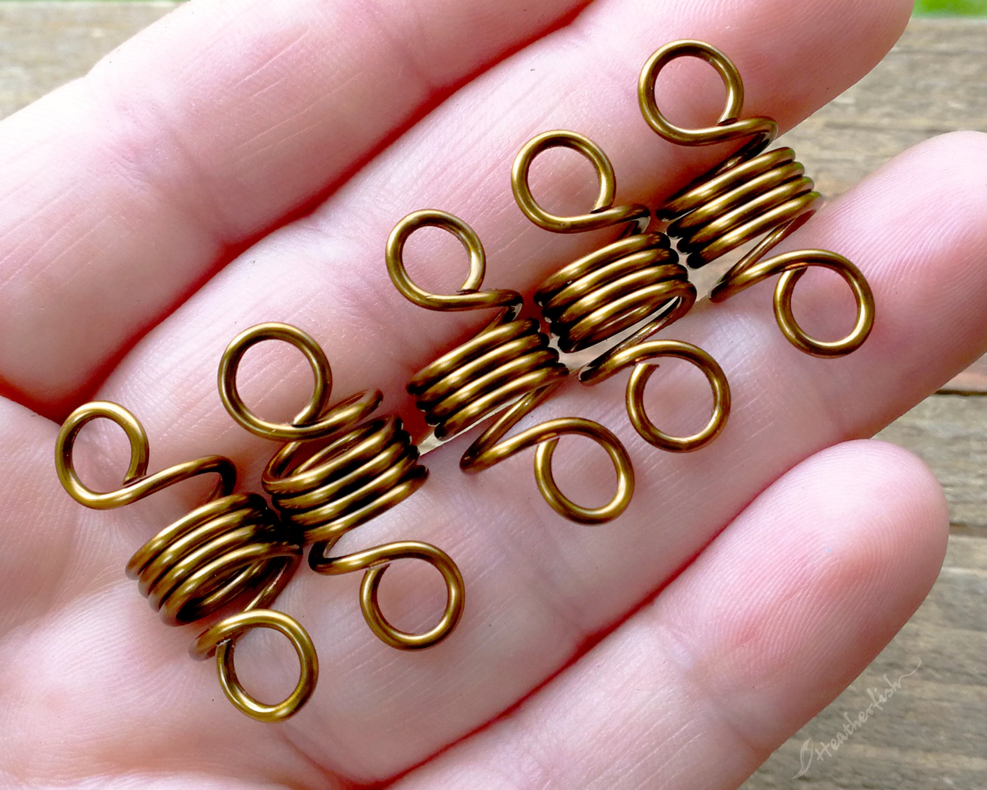 A set of 5 hair beads held in a hand to show scale.