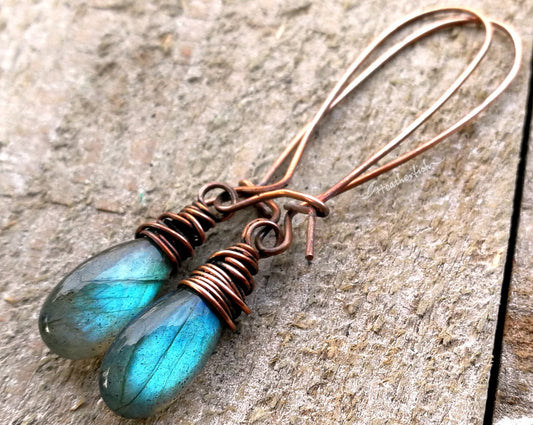 A pair of labradorite earrings on a whitewashed wood background.