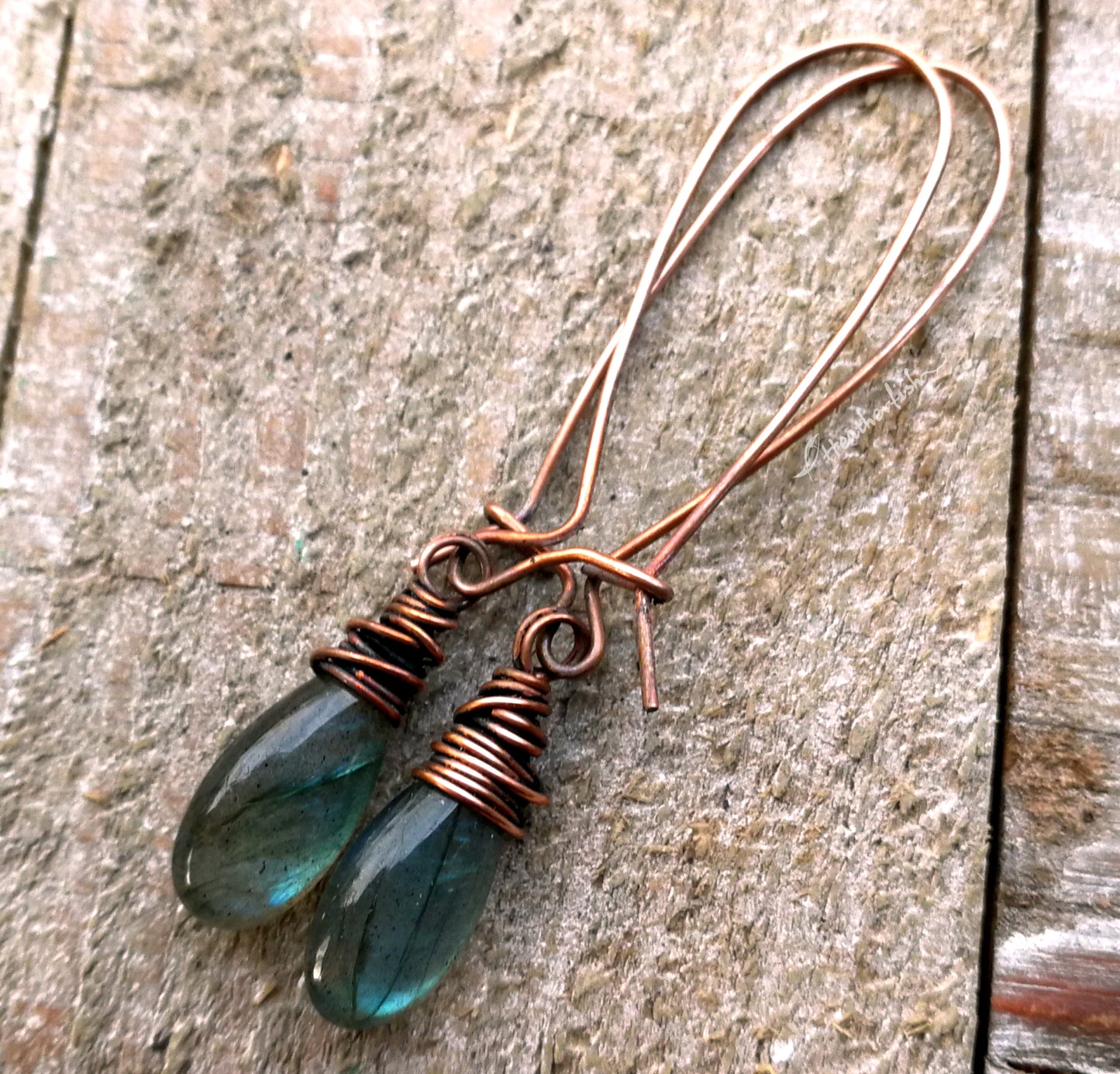 A pair of labradorite earrings on a whitewashed wood background.