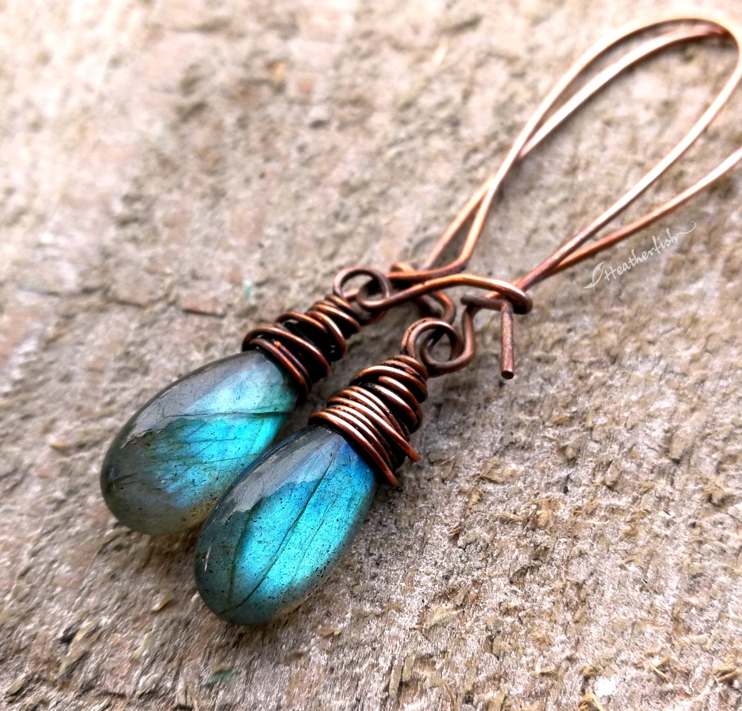 A pair of labradorite earrings on a whitewashed wood background.