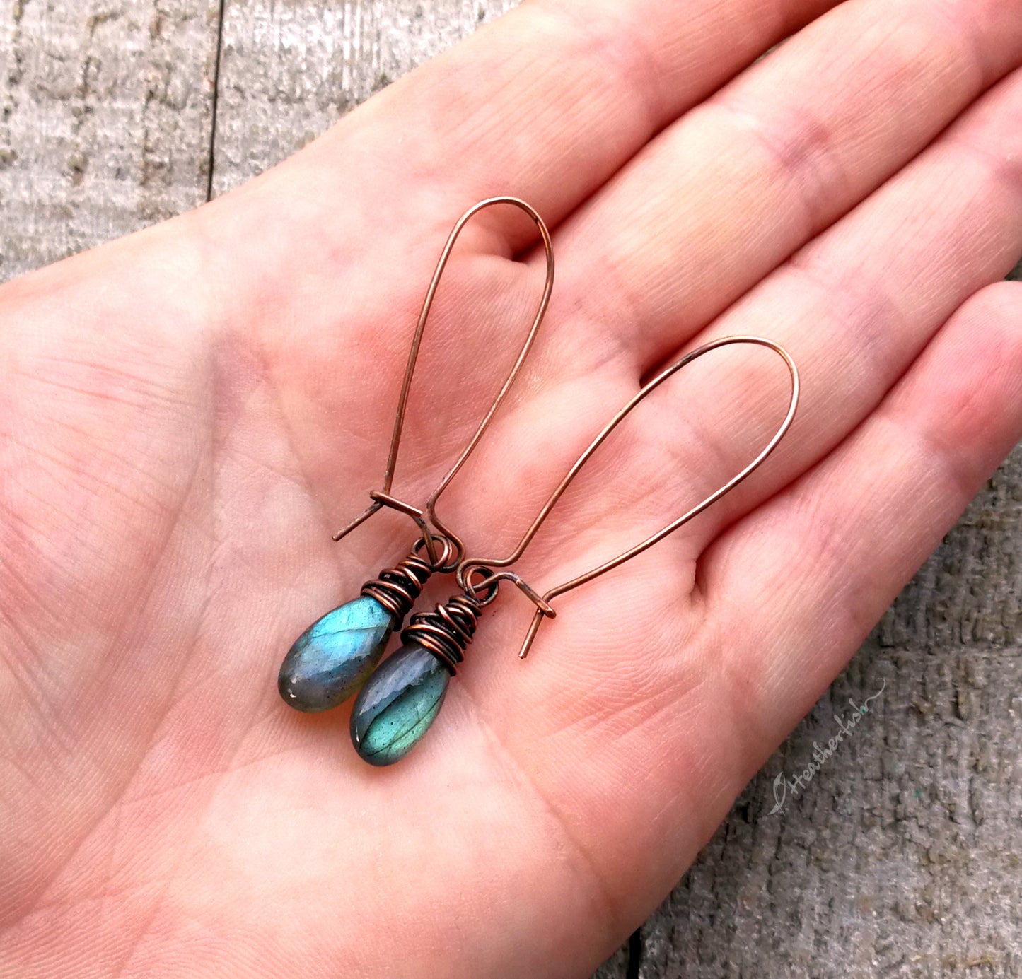 A pair of labradorite earrings held in a hand to show scale.