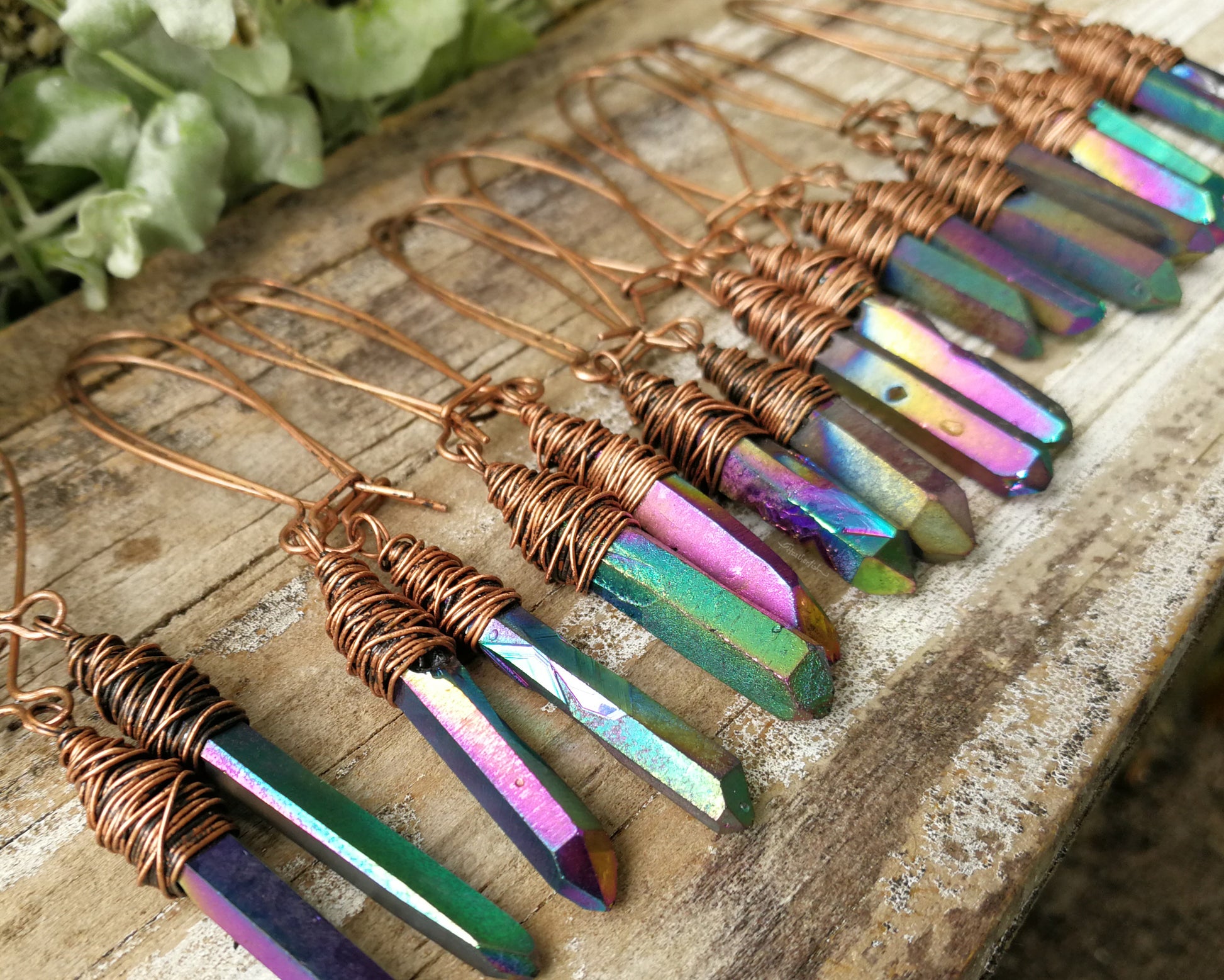 Many pairs of rainbow titanium quartz earrings on a wood background.