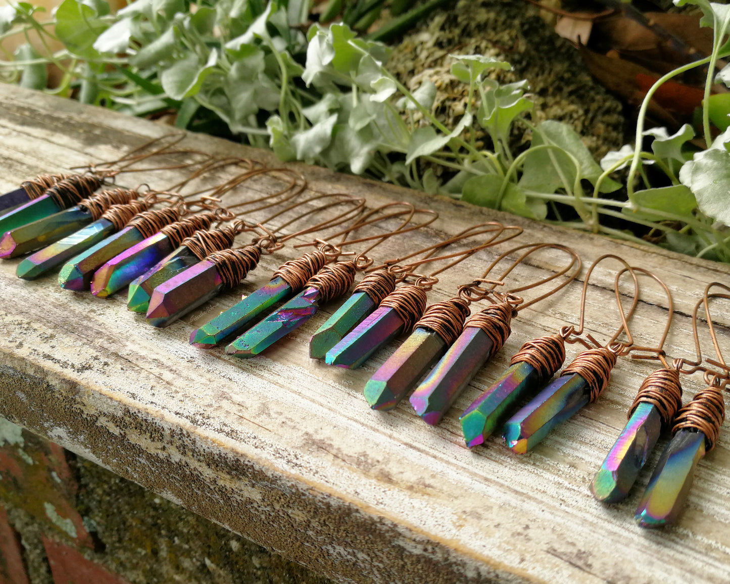 Many pairs of rainbow titanium quartz earrings on a wood background.