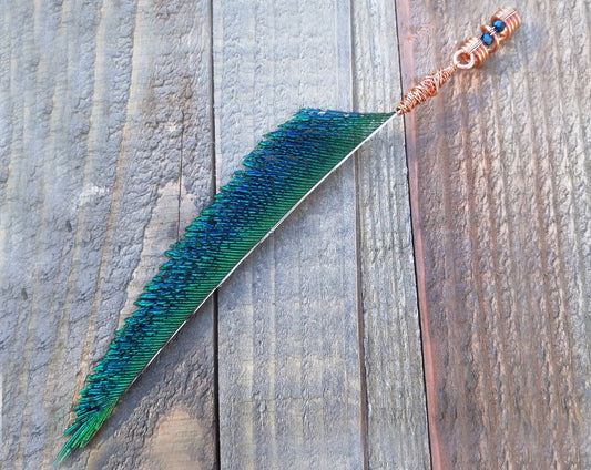 A peacock feather blade dread bead on a wood background.