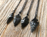 Black obsidian arrowhead necklace shown on wood background.