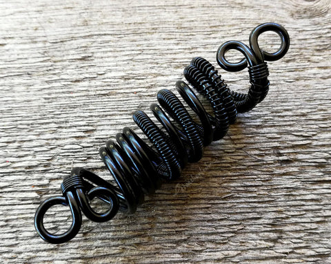 A close up of a Black Woven Dread Bead on a wooden background.