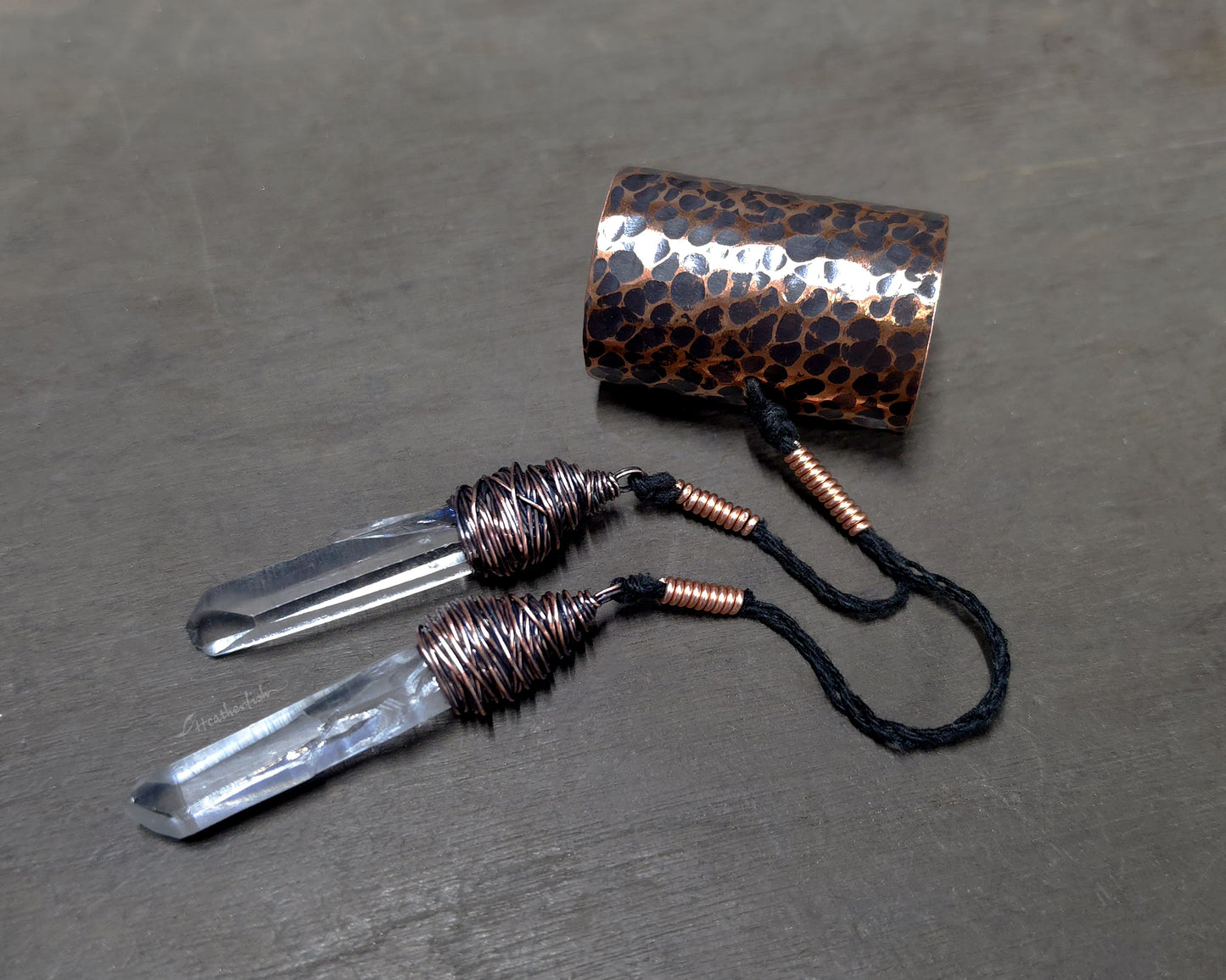 Two Clear Arkansas quartz crystals attached to a hammered copper hair cuff on a wood surface.