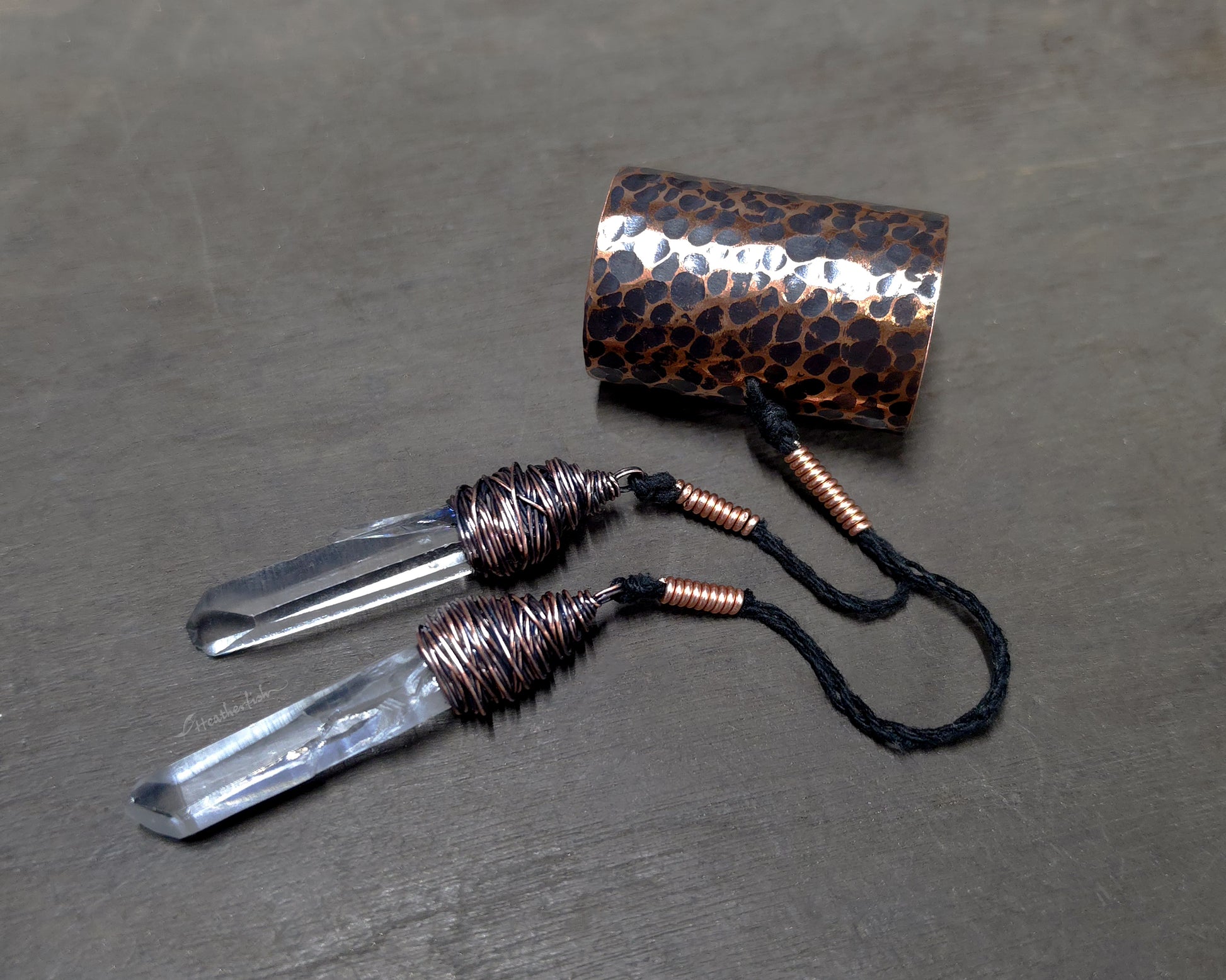 Two Clear Arkansas quartz crystals attached to a hammered copper hair cuff on a wood surface.