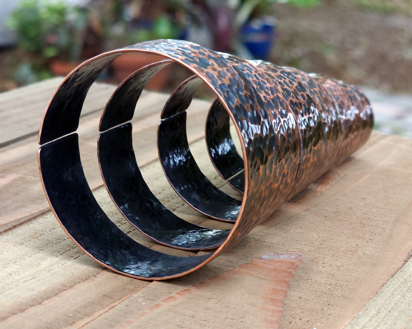 Copper hair cuffs lined up on a wood surface to show size options.