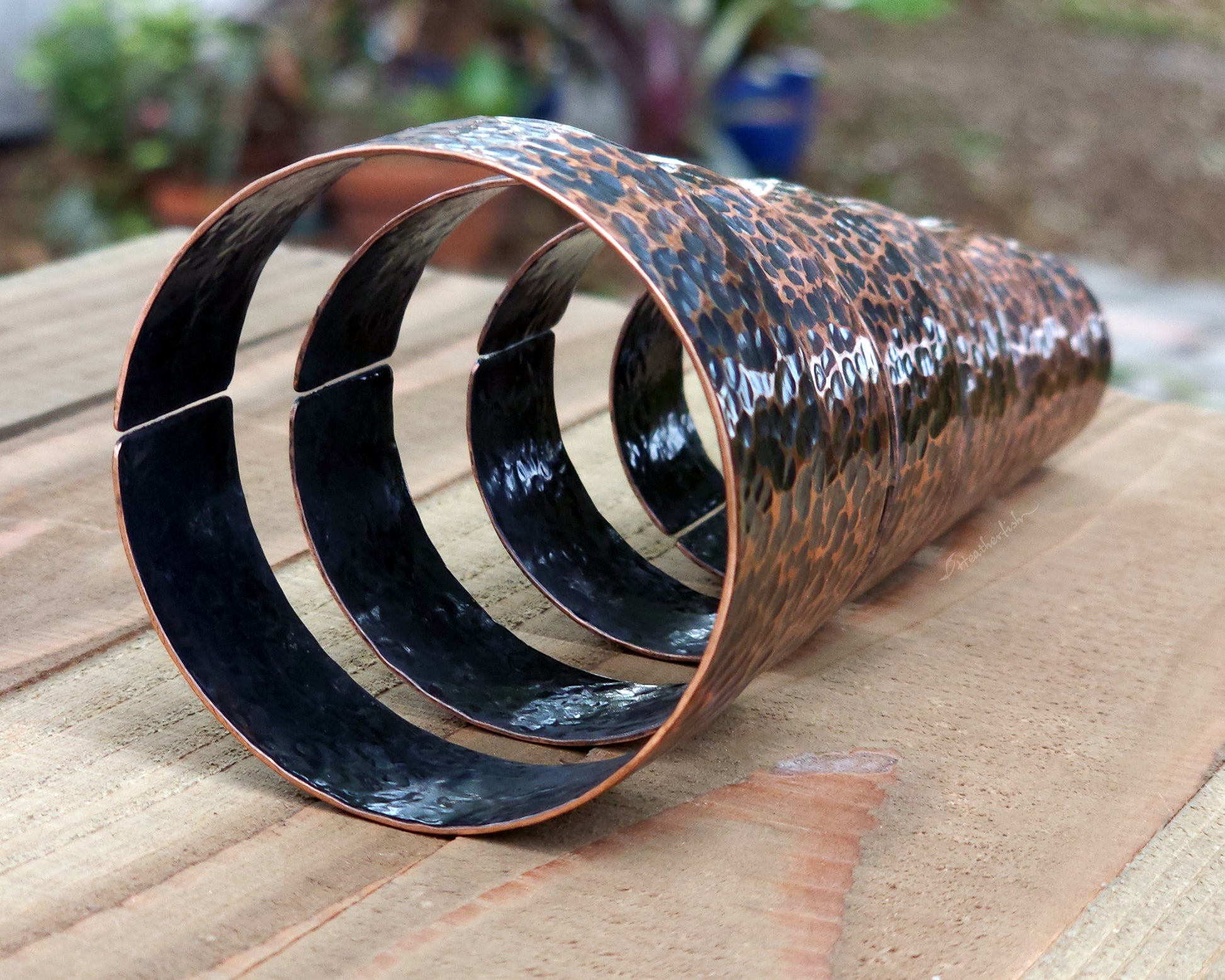 Copper hair cuffs lined up on a wood surface to show size options.