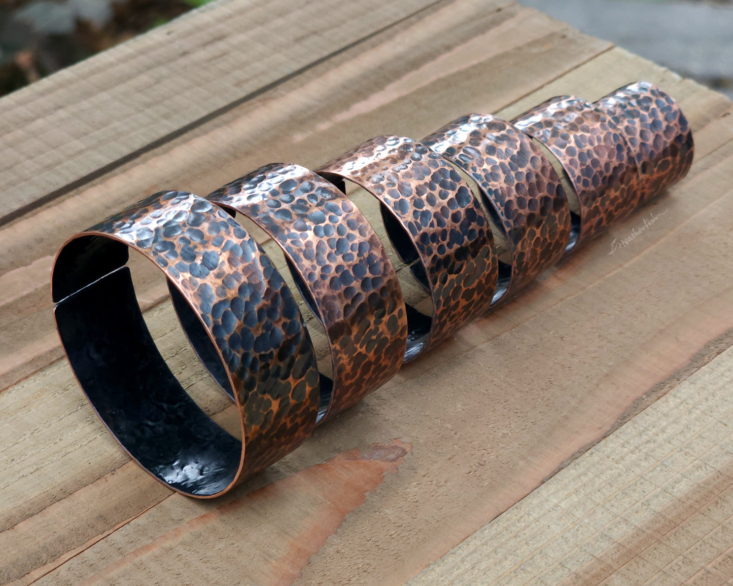 Copper hair cuffs lined up on a wood surface to show size options.