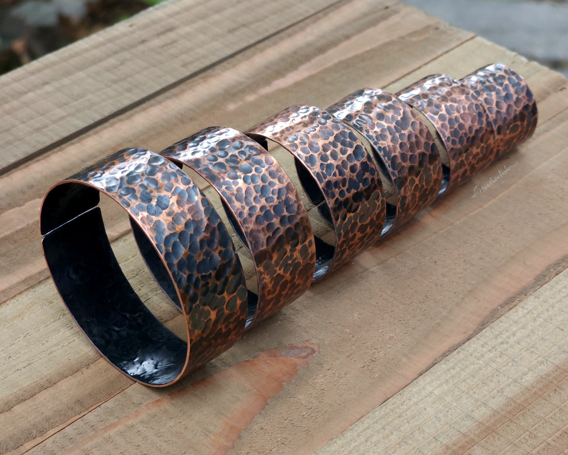Copper hair cuffs lined up on a wood surface to show size options.