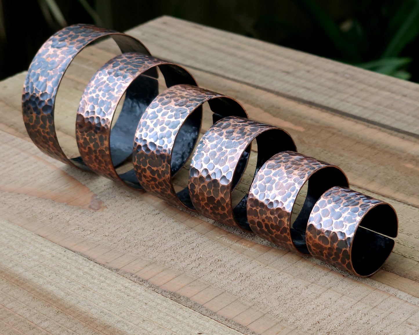 Copper hair cuffs lined up on a wood surface to show size options.
