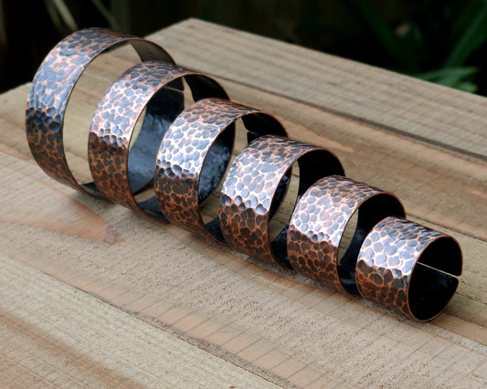 Copper hair cuffs lined up on a wood surface to show size options.