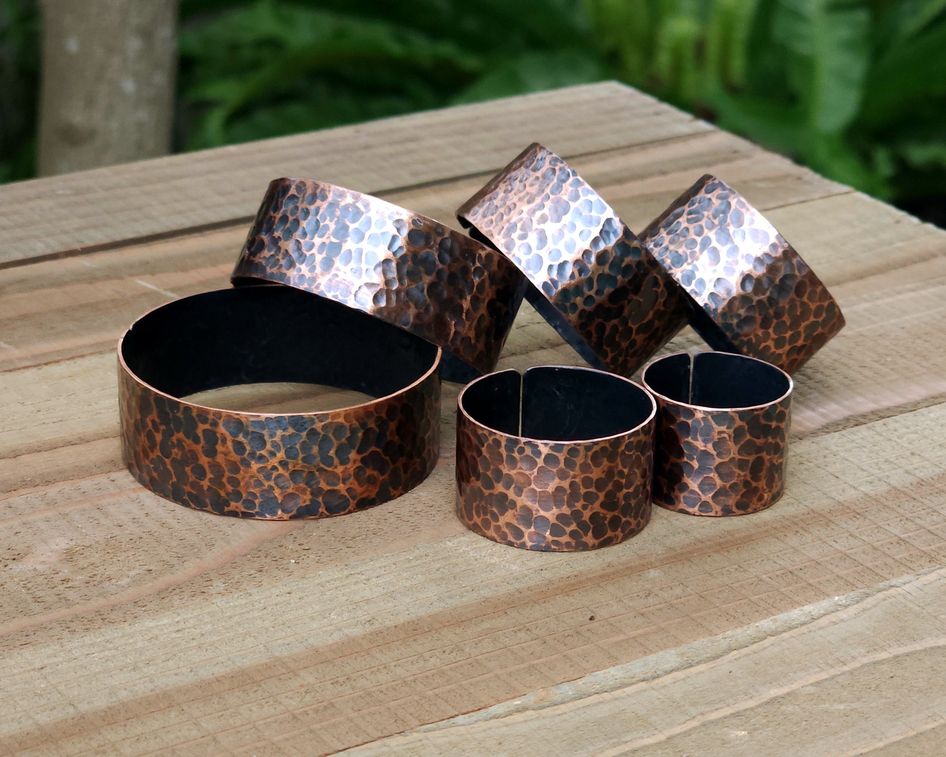 Copper hair cuffs lined up on a wood surface to show size options.