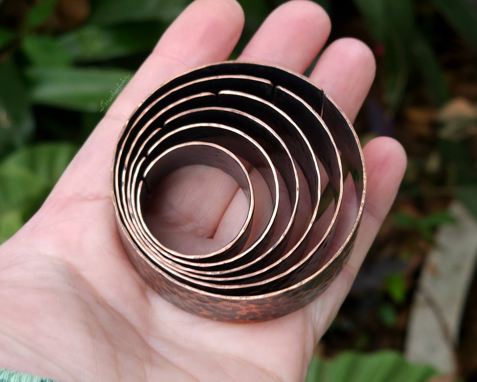 Copper hair cuffs held in hand with a natural background.