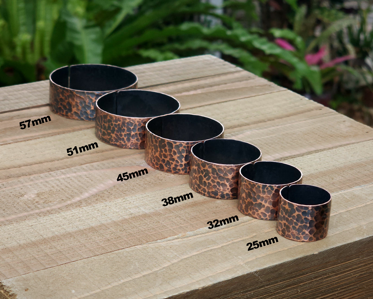 Copper hair cuffs lined up on a wood surface to show size options.