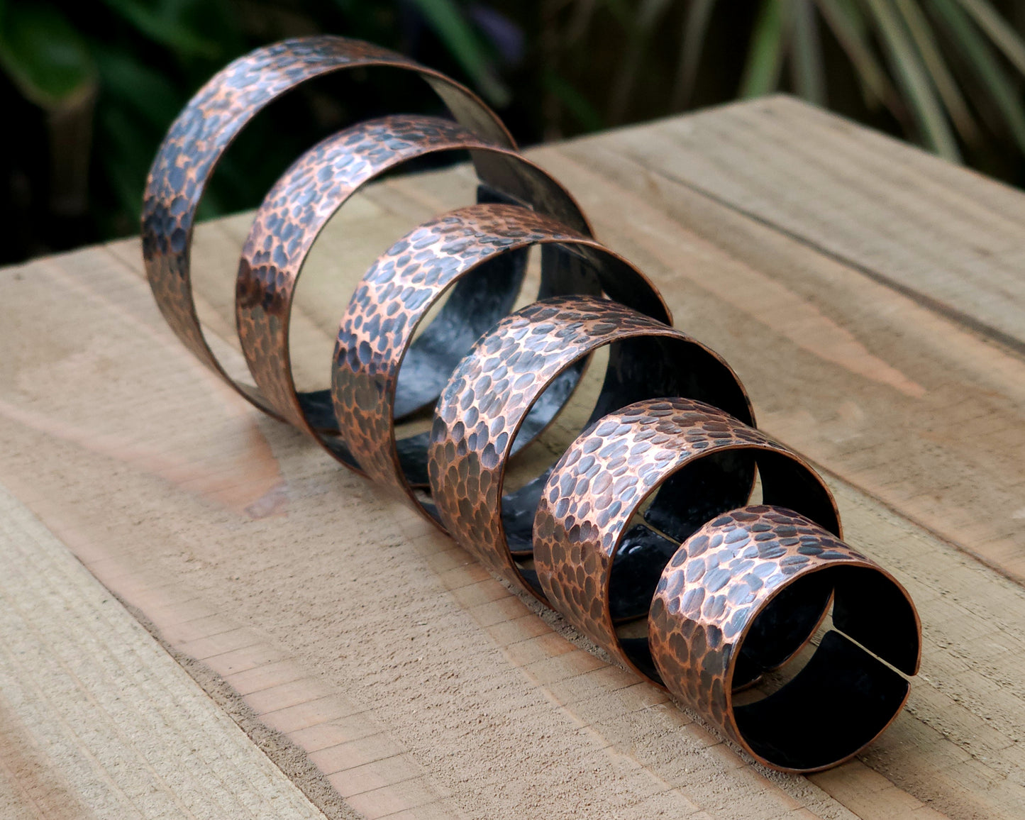 Copper hair cuffs lined up on a wood surface to show size options.