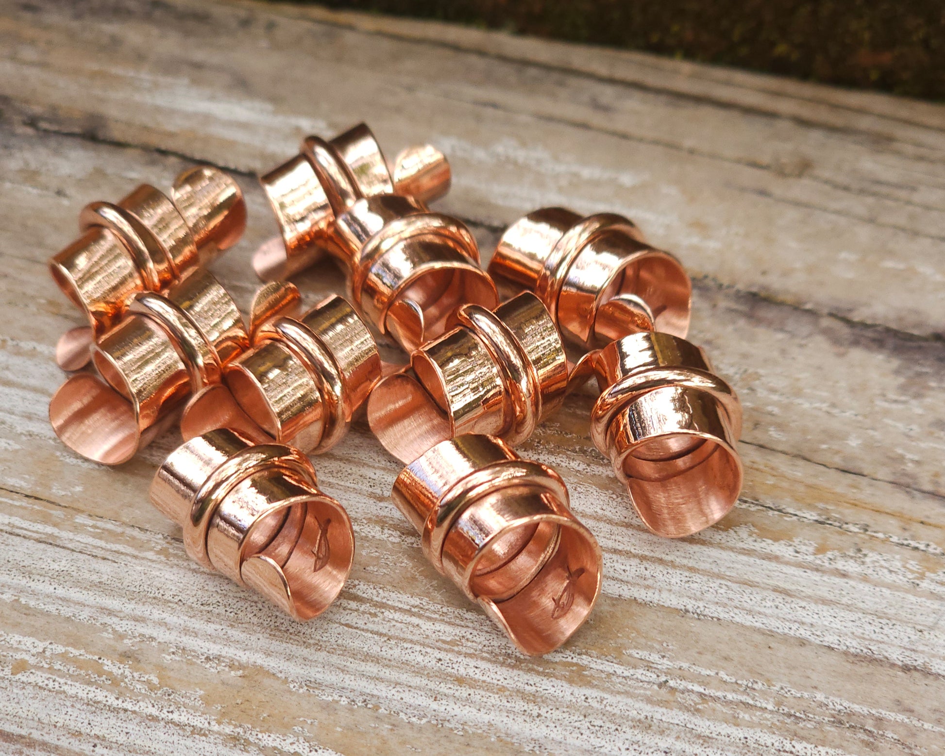 Copper hair jewelry for locs, dreadlocks, braids, or beards, stylized with a center ring and flattened ends, displayed on a wood background.