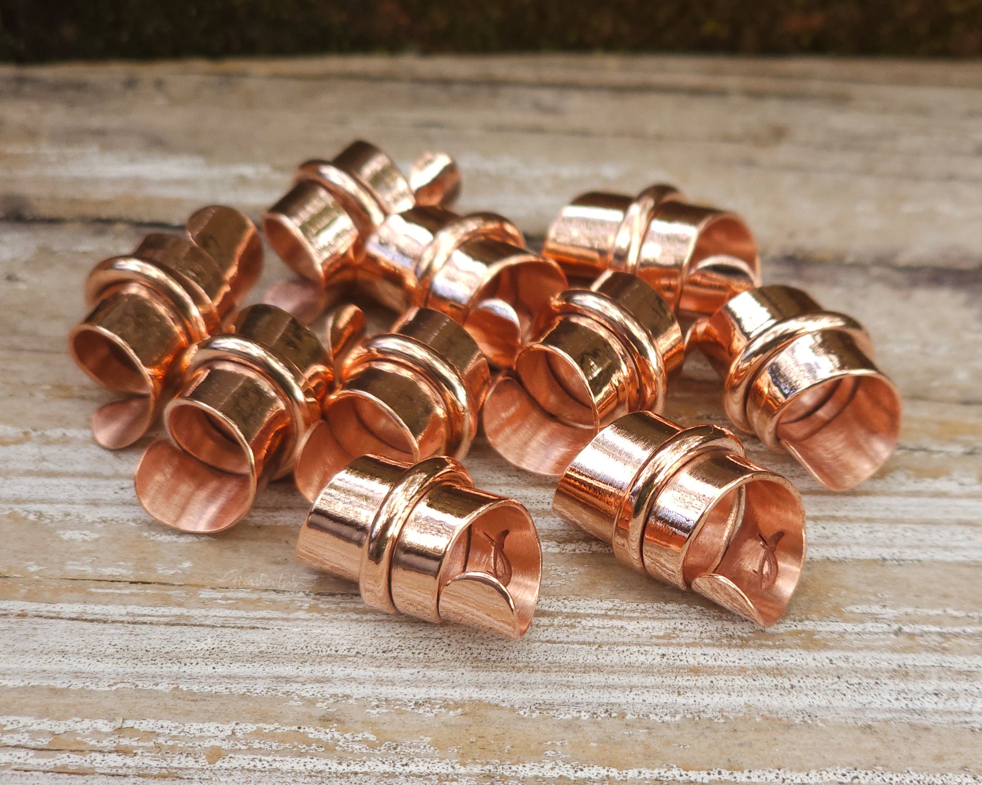 Copper hair jewelry for locs, dreadlocks, braids, or beards, stylized with a center ring and flattened ends, displayed on a wood background.